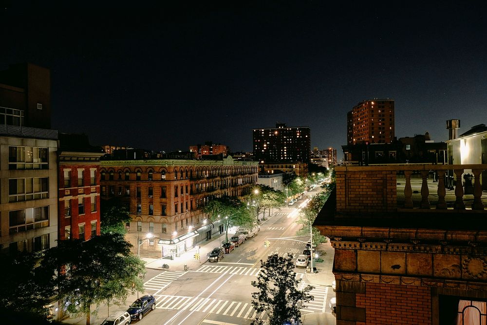 Rooftop view of a quiet city at night. Lights illuminate the street and tall buildings in the distance.