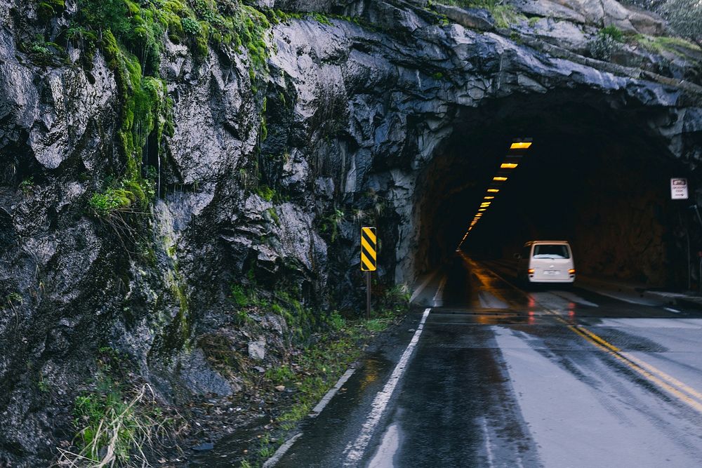 A car drives into a lit entrance of a tunnel that goes through a mountain.