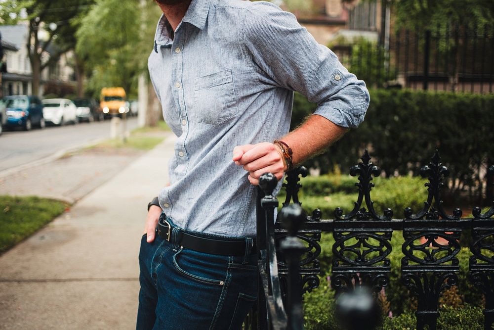 A man wearing a button down shirt and jeans leaning against an iron fence