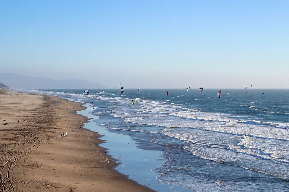 Beach with people flying kites in the ocean.