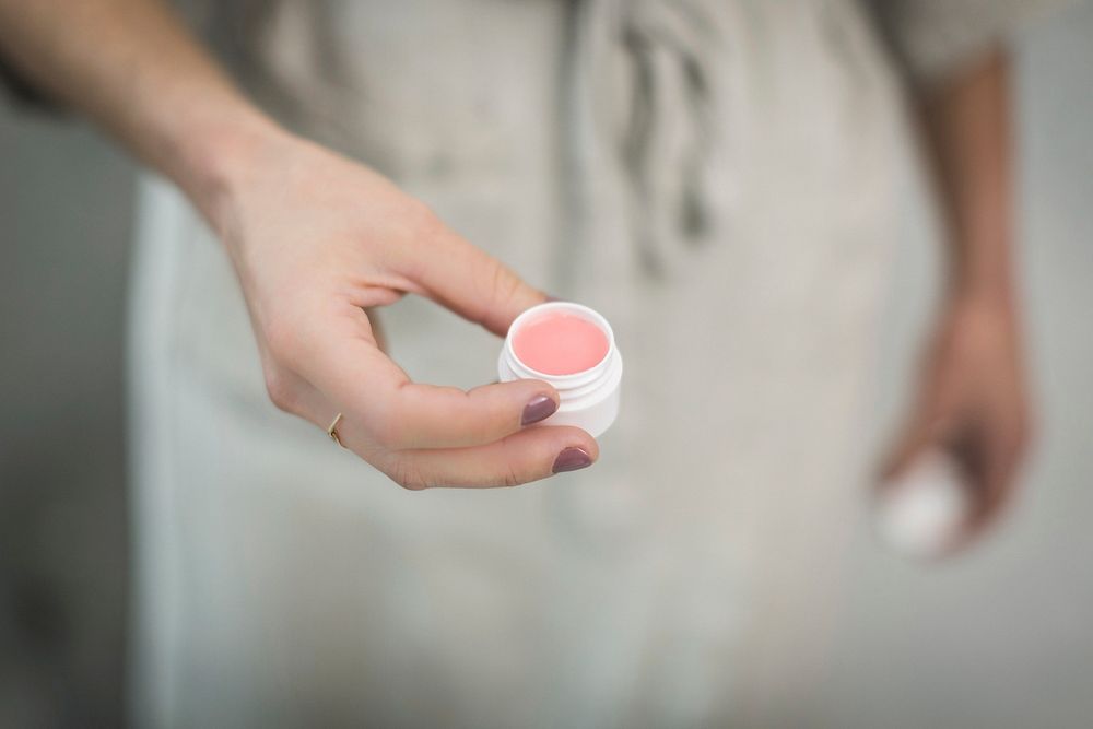 Close up of woman holding jar of pink homemade lip balm.