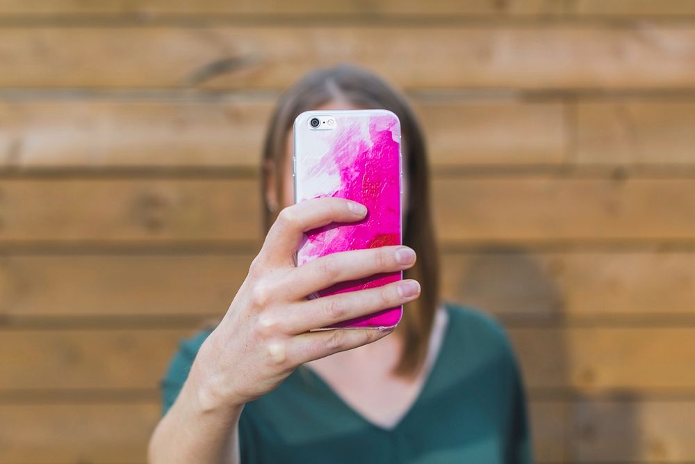 Woman holding up iPhone with white and pink case.