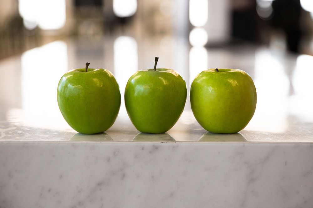 Three green apples on a marble counter top.