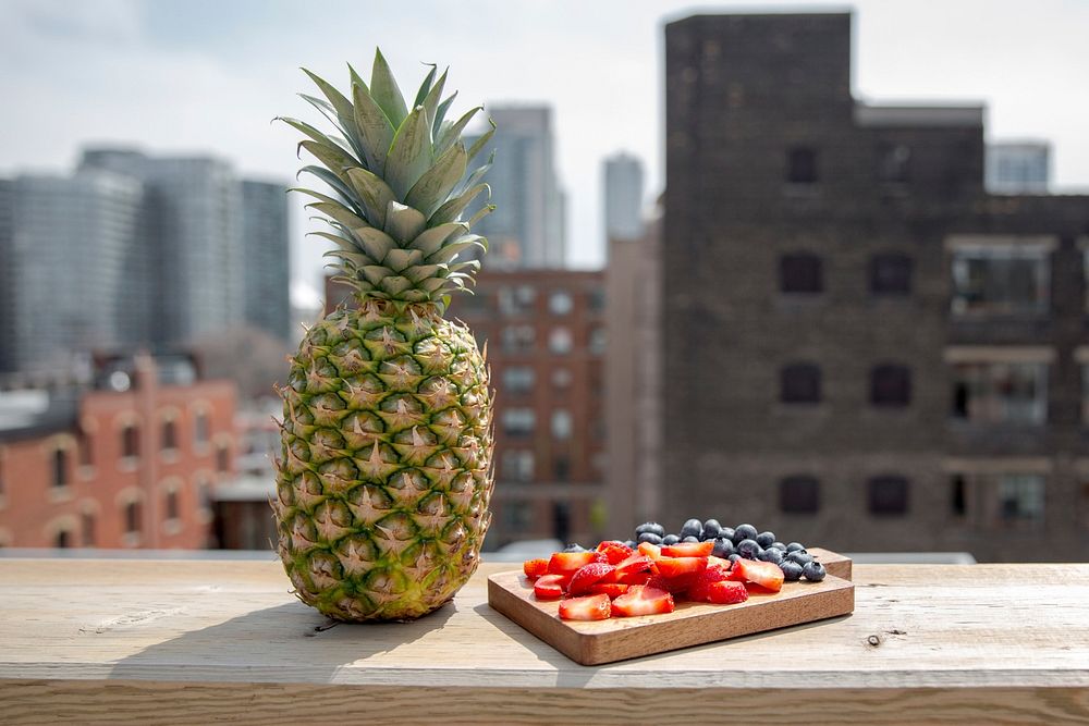 Pineapple, strawberries, and blueberries sitting outside on a patio with a city view in the background.