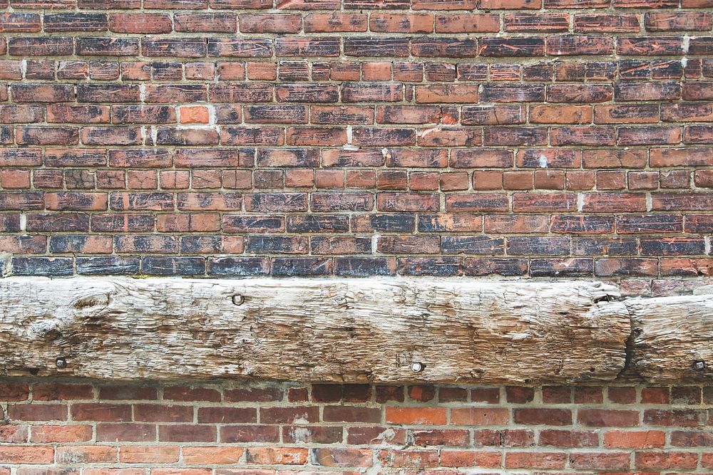 Worn down brick wall with an aged wood beam and newer brick below.