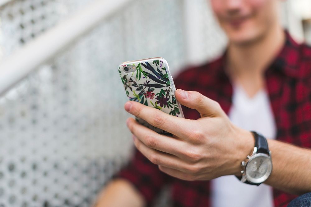 Young man checking iPhone with leaves and flowers print case.