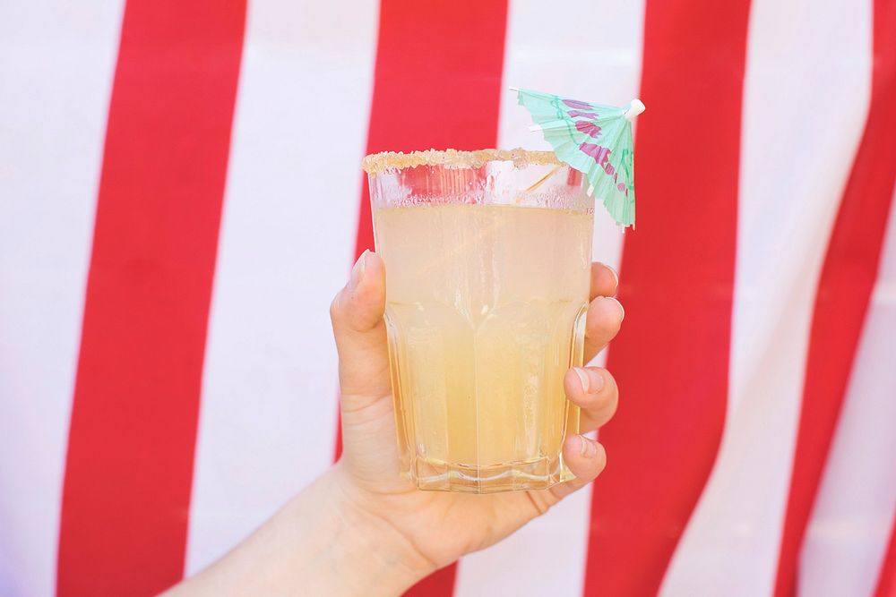 Free hand holding summer cocktail in front of red and white striped background photo, public domain beverage CC0 image.