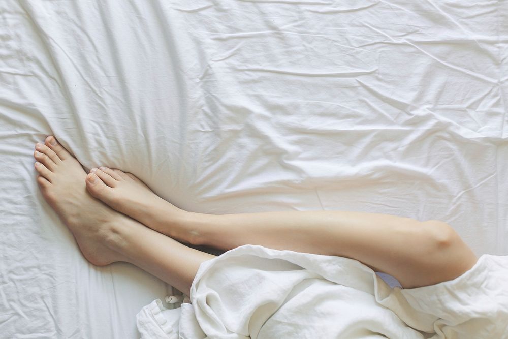 A pair of legs rest in a soft bed with white sheets.