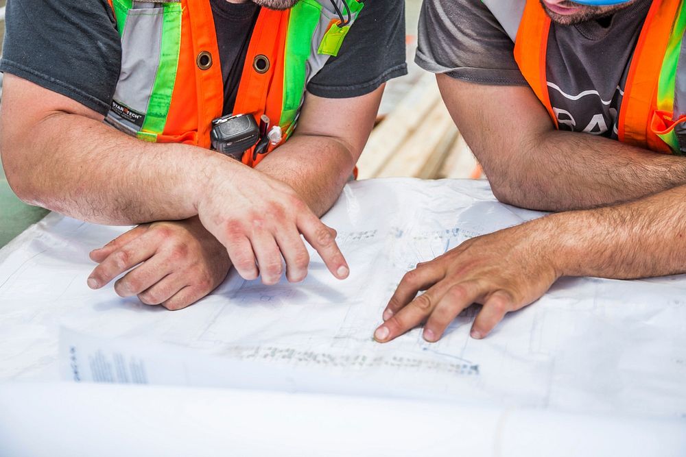 The hands of construction workers going over blueprints on a construction site.