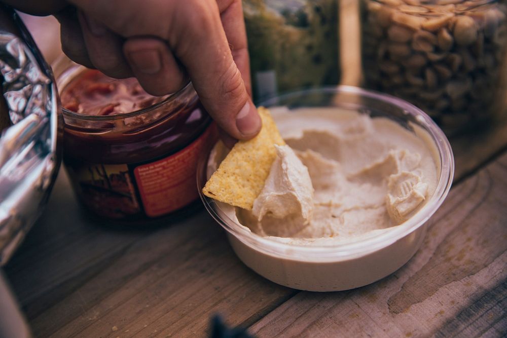 Free tortilla chip in hand dipping in hummus image, public domain food CC0 photo.