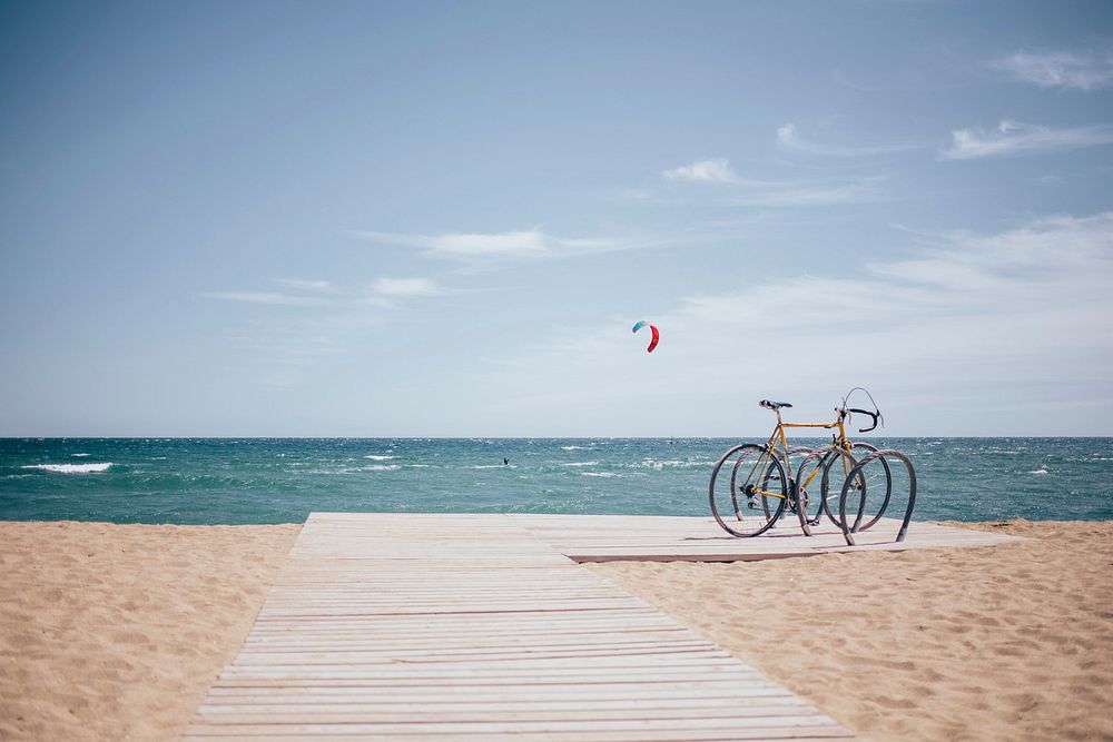 A bike parked at the beach with a kite surfer in action in the background.