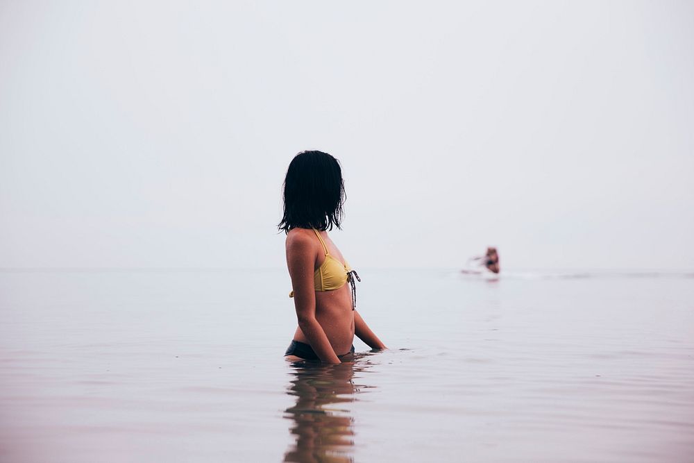 A woman looks away as she wades in still water.