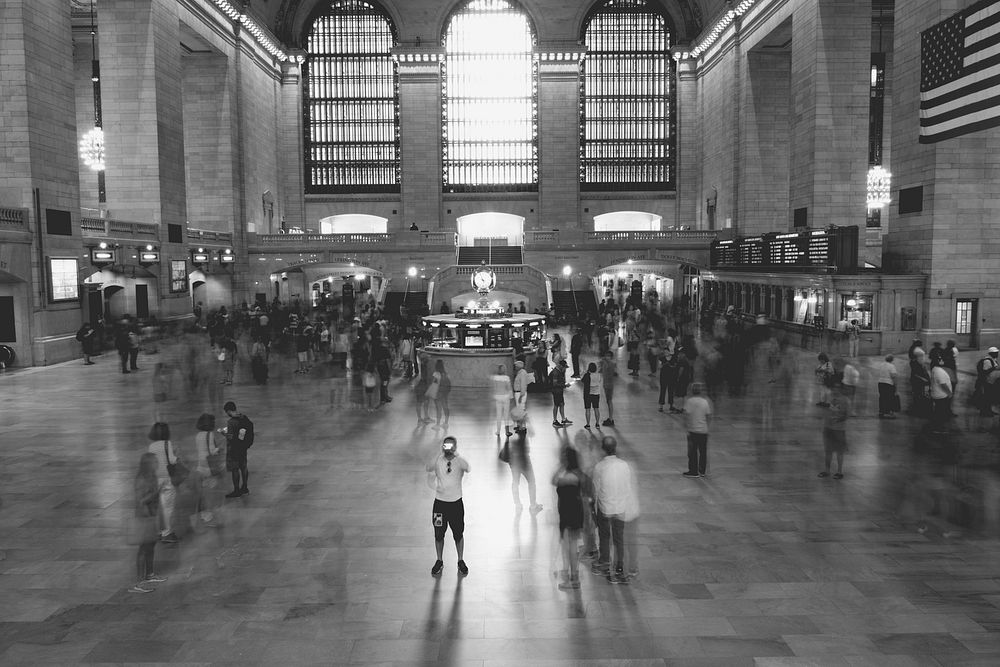 Black and white image of Grand Central train station with blurry and moving bodies of people as they walk through.