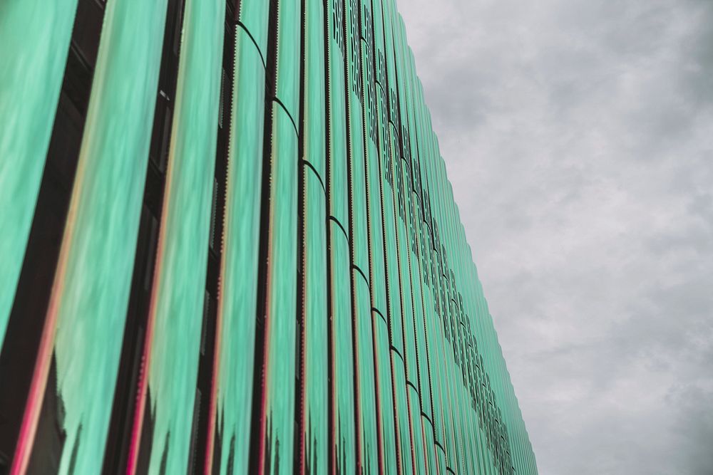 A modern building with green vertical glass stands tall beside a cloudy sky.