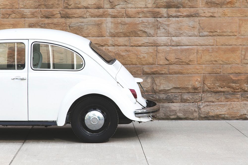 The back half of a white bug shaped car parked beside a brick wall.