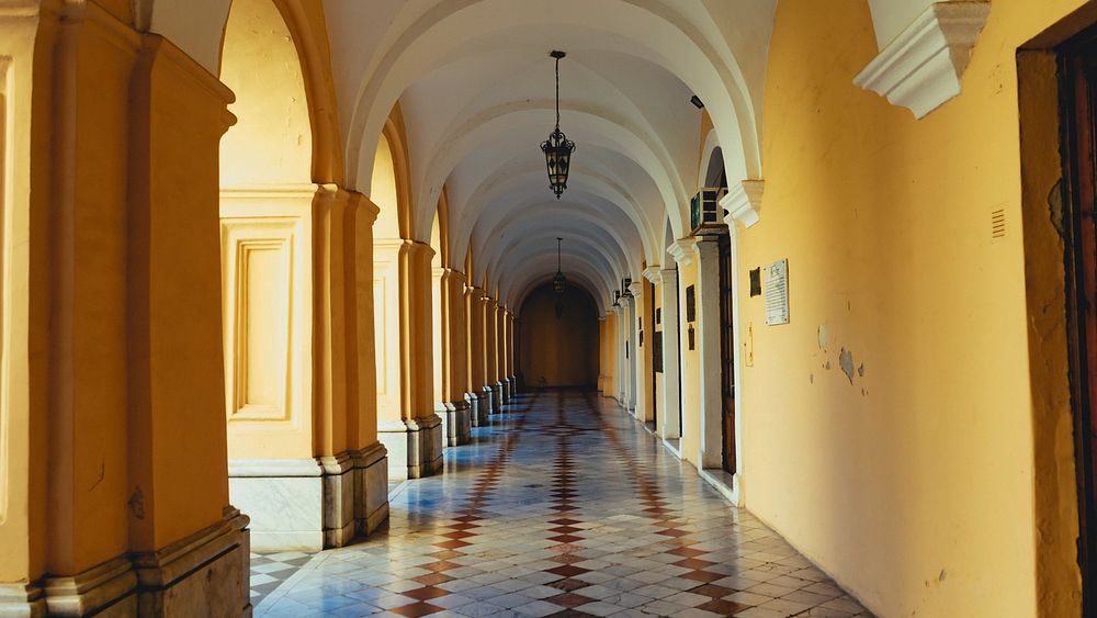 An outdoor hallway with arched ceilings, yellow walls, and tiled floor.
