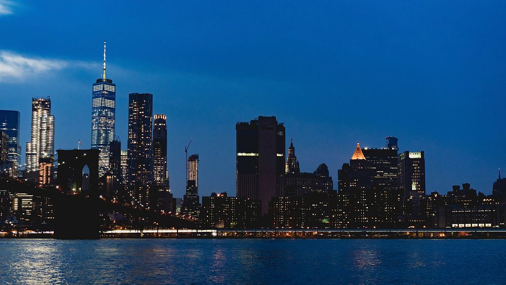 New York City skyline at night with the Brooklyn Bridge stretching over the water, free public domain CC0 photo.