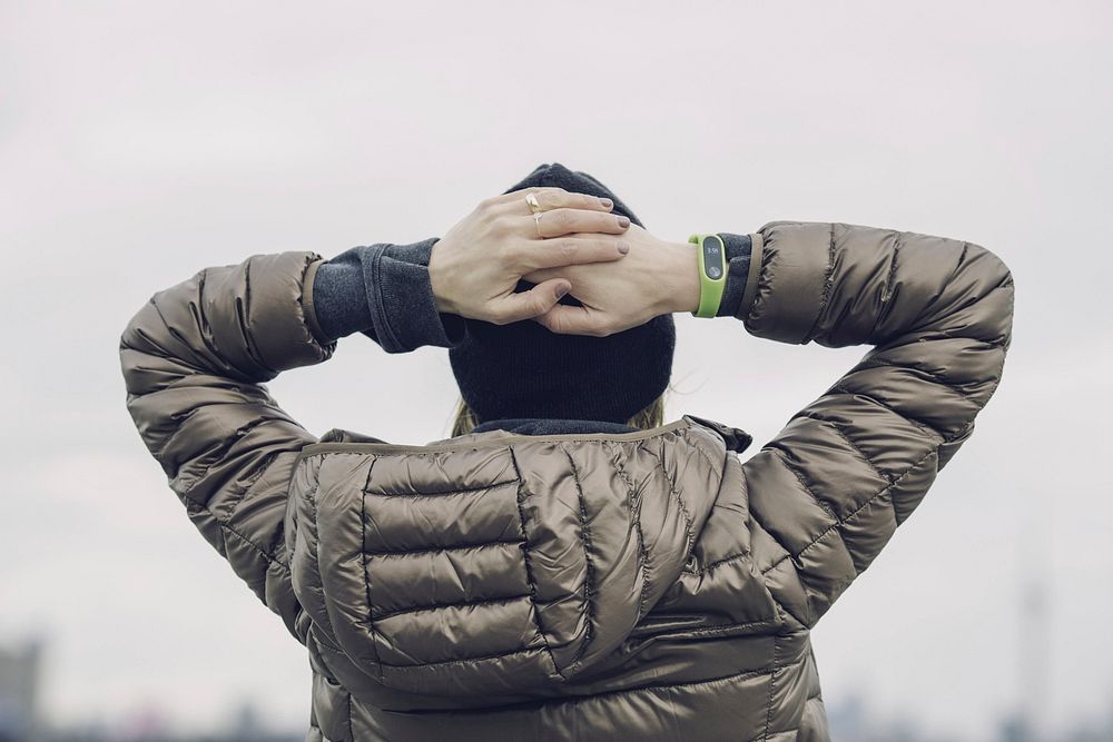 Woman relaxed and looking at the horizon; she's wearing winter a brown winter jacket and fitness tracker.