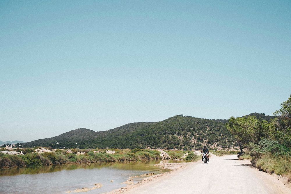 Motorcycle rides on an open road past hills and fields.