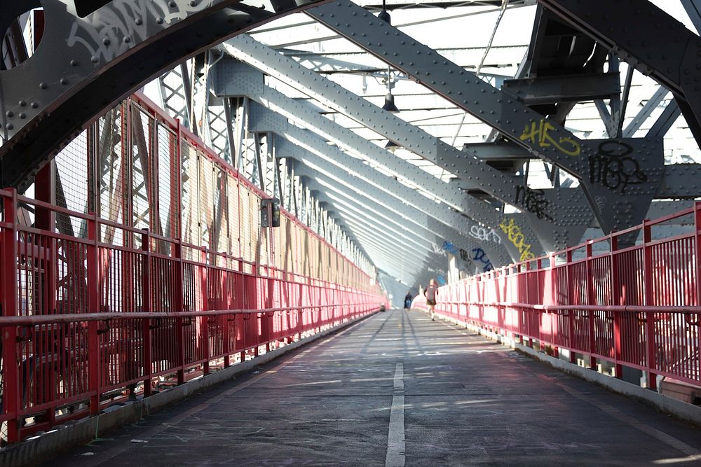 Walking bridge in New York with a red fence and thick grey beams on angles above.