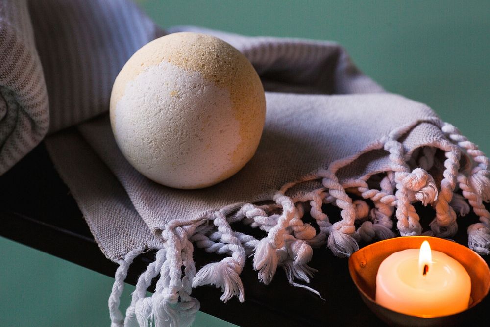Yellow and white bath bomb on purple scarf by candle.