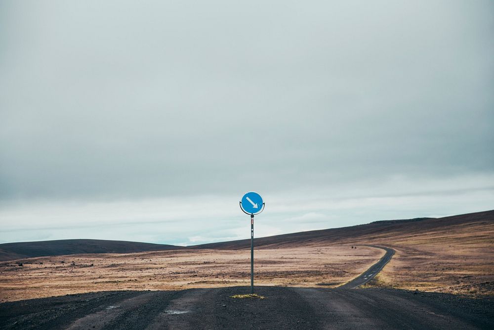 A lone sign managing the lone dark dirt road through the hillside of Iceland, free public domain CC0 image.
