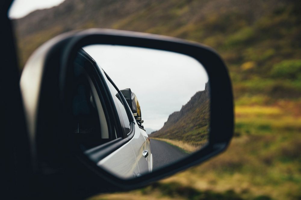 Mirror view from a moving truck down the road, next to steep hills. An adventurous drive for sure!