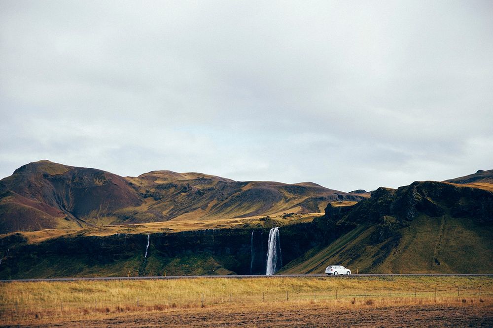 A waterfall cascades off a cliff beside an Icelandic highway. Nature meets man at the edge of a beautiful natural landscape.