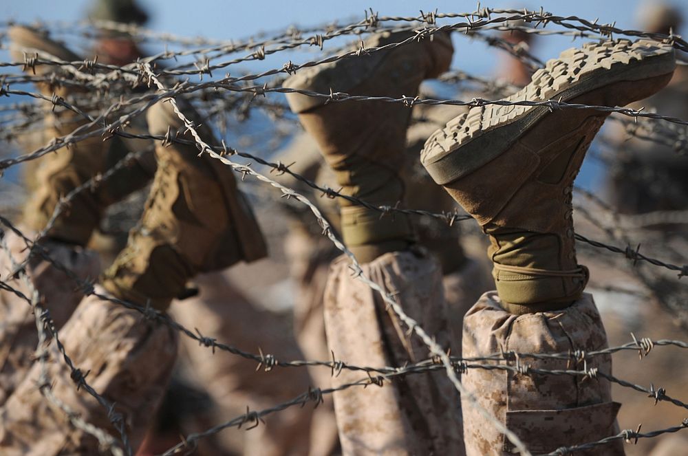 Marines with Company E, Battalion Landing Team 2/4, 11th Marine Expeditionary Unit, use their boots to lift barbed wire…