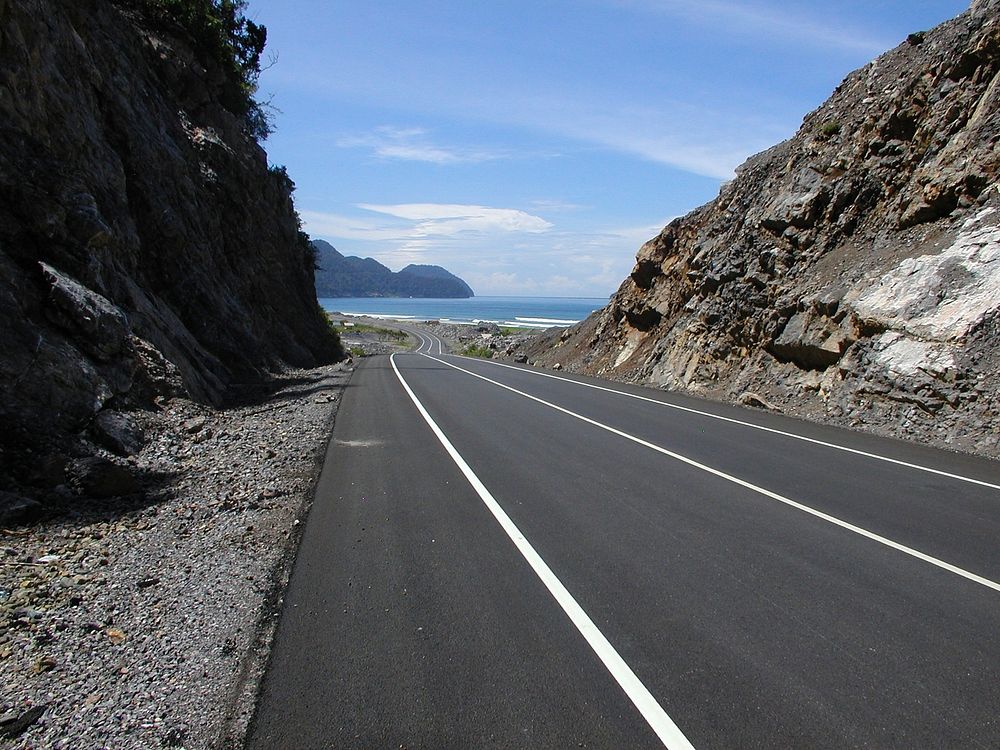 Completed section of the highway penetrating dense rock and emerging to a beautiful view of the Indian Ocean. Original…