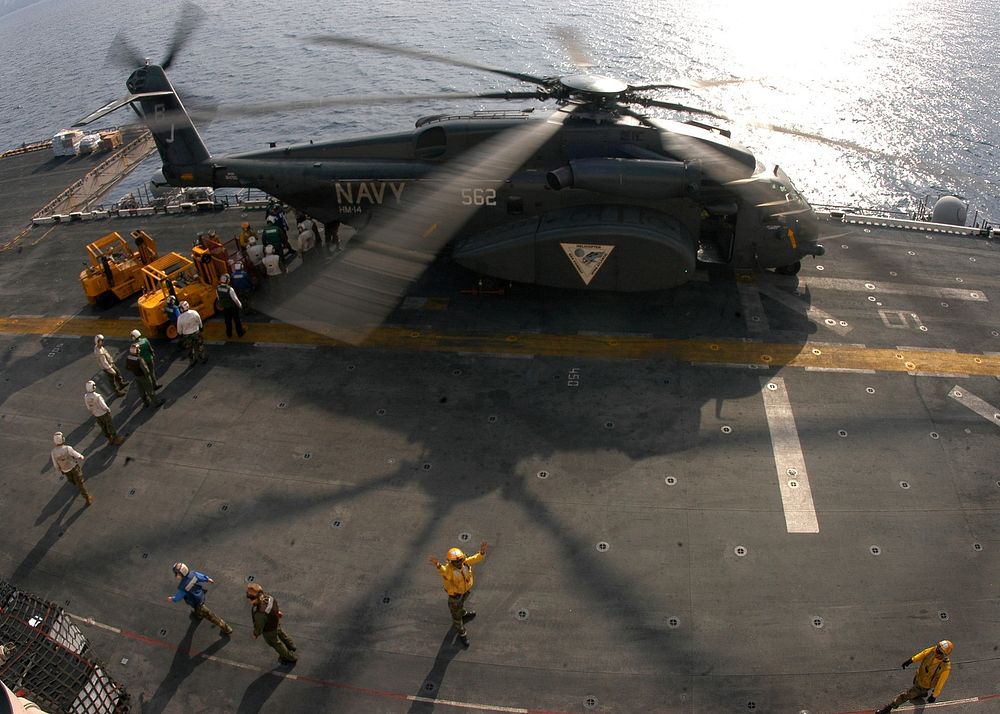 U.S. Navy flight deck personnel unload supplies from an MH-53E Sea Dragon helicopter assigned to Helicopter Mine…