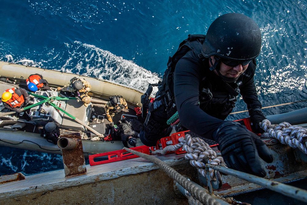 U.S. Navy Damage Controlman 2nd Class Patrick Trandem, from Marion, Iowa, climbs a pilot’s ladder from a rigid-hull…