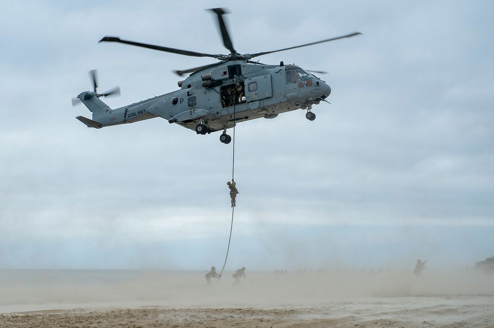British Royal Marines fast rope from a British Merlin helicopter during a distinguished visitor (DV) day amphibious landing…