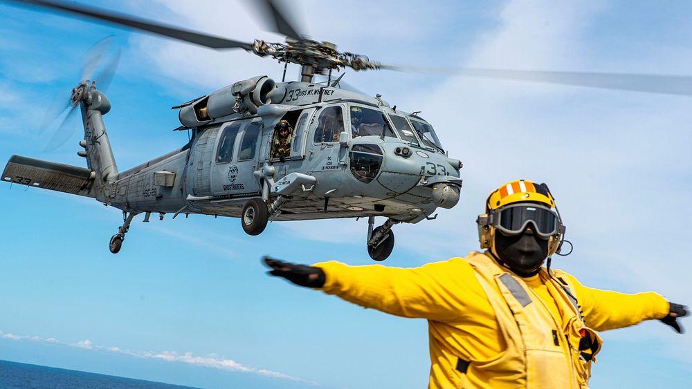 MEDITERRANEAN SEA (May 06, 2021) A Military Sealift Command civil service mariner guides an MH-60 Sea Hawk helicopter…