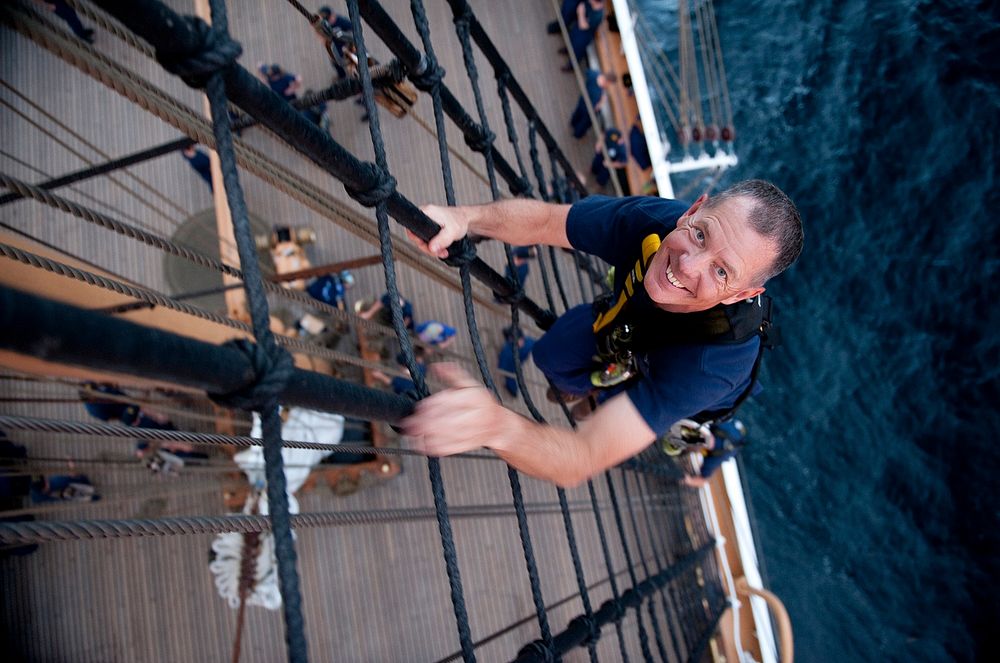 U.S. Coast Guard Master Chief Petty Officer Rex Gunderson poses for a photo while climbing the rigging aboard the Coast…