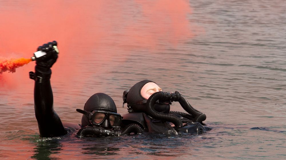 A U.S. Navy Basic Underwater Demolition/SEAL (BUD/S) candidate waves a flare during a simulated dive casualty drill while…