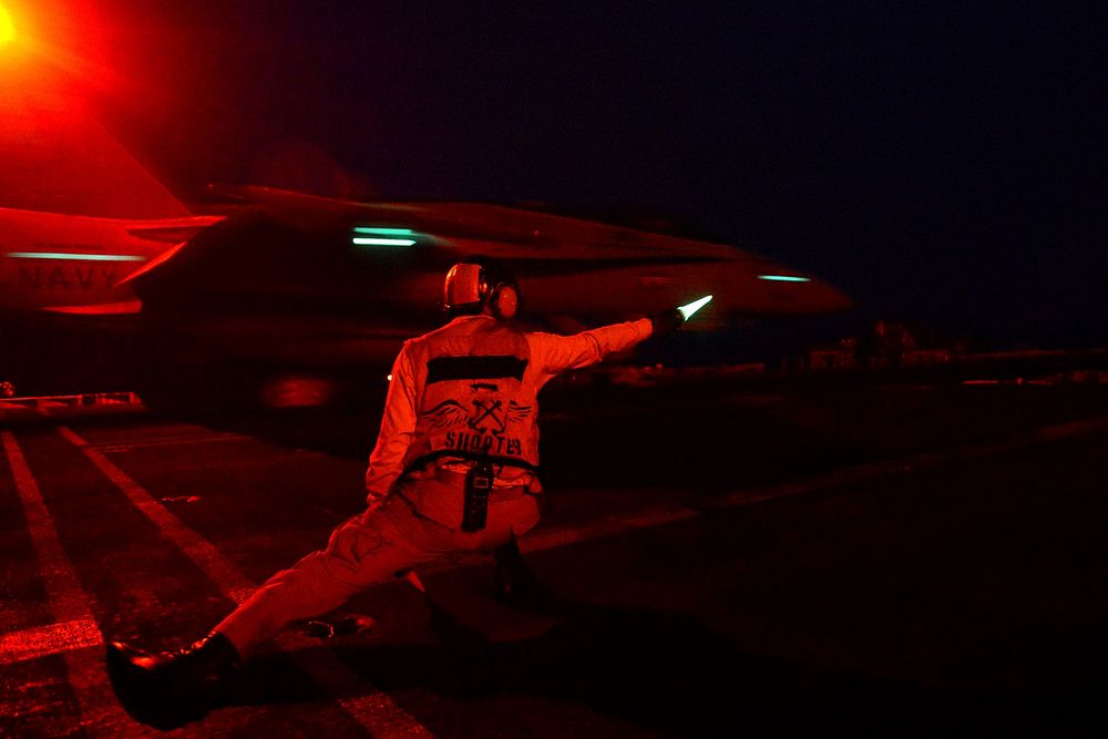 A catapult and arresting gear officer signals for the night launch of an aircraft from the aircraft carrier USS John C.…