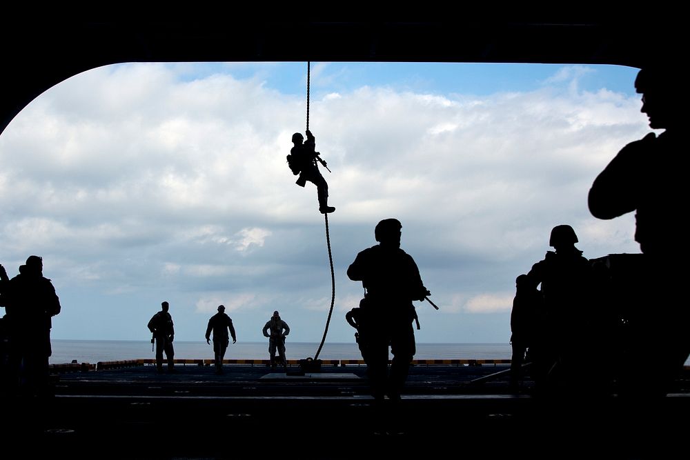 U.S. Marines with the 26th Marine Expeditionary Unit (MEU) enter the hangar bay after fast-roping from the flight deck…