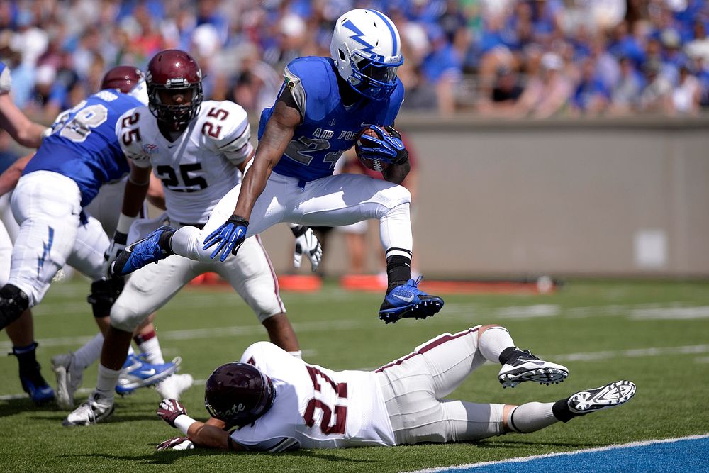 U.S. Air Force Academy (USAFA) running back Jon Lee, center, leaps into the end zone for a touchdown during a game against…