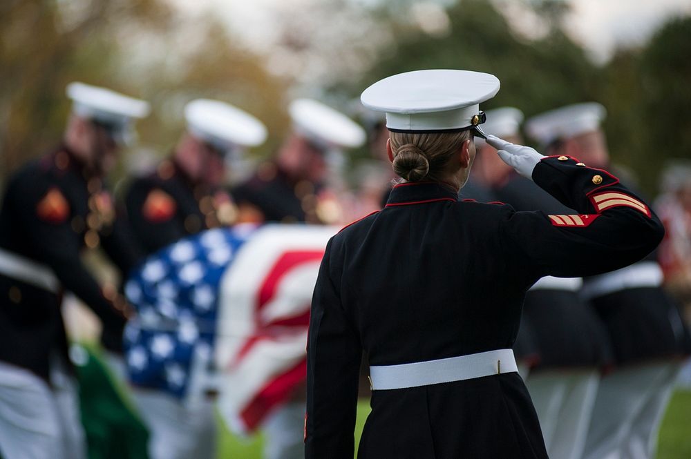 U.S. Marine Corps Sgt. Katie Maynard salutes as a casket is lowered during a funeral ceremony at Arlington National Cemetery…