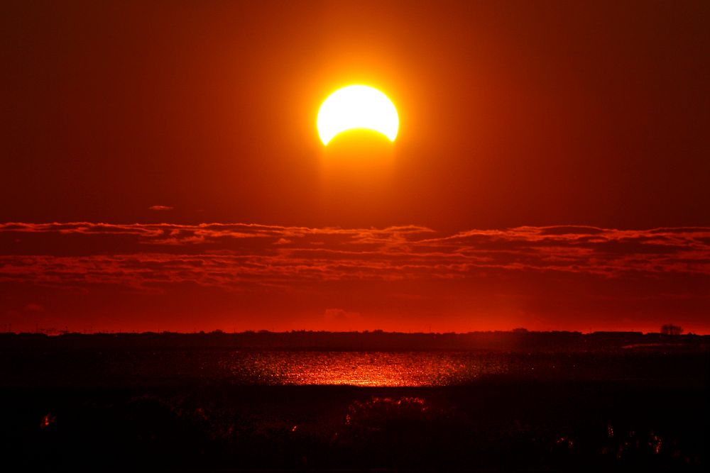 Partial solar eclipse with reflection in water. Original public domain image from Flickr