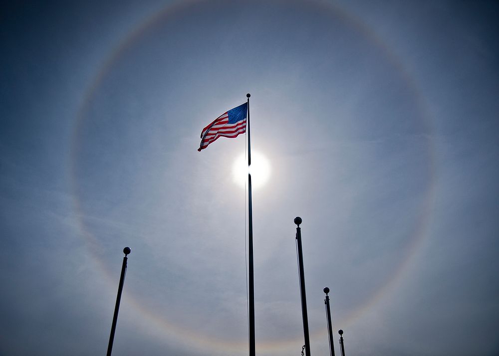 A solar halo illuminates the sky behind an American flag flying outside Building 1 at Eglin Air Force Base, Fla., in the…