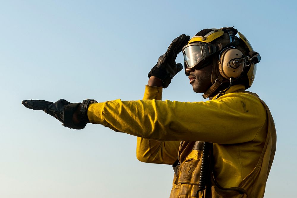 U.S. Navy Aviation Boatswain's Mate (Handling) 2nd Class Marcus Stewart directs a helicopter on the flight deck of the…