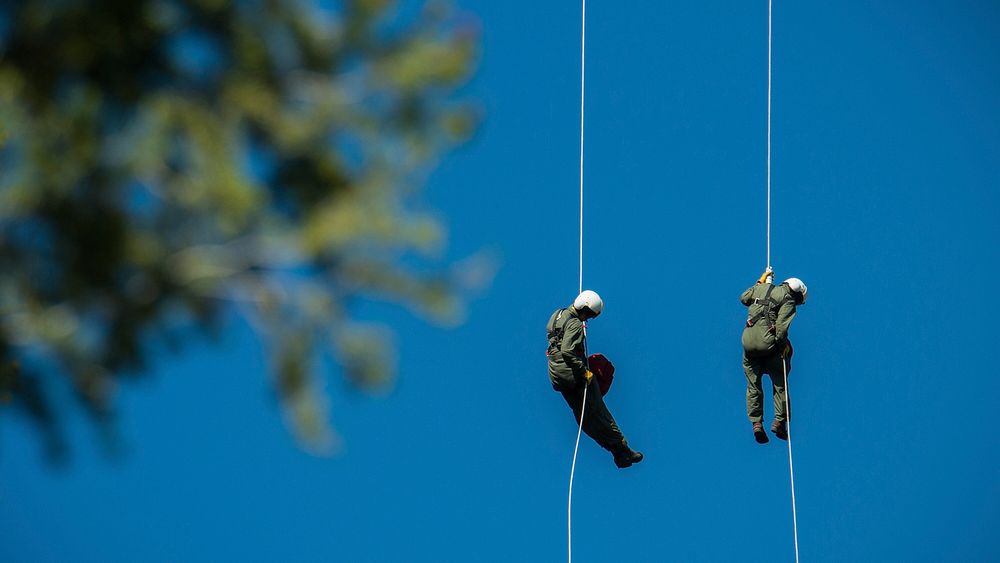 Veteran wildland firefighter rappellers use various techniques to negotiate the wind from the helicopter rotor blades above…