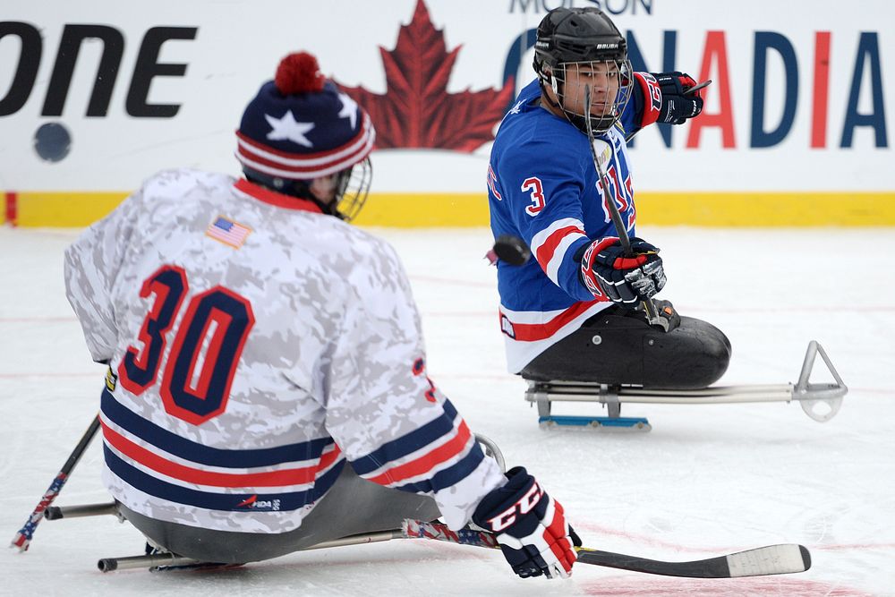 Ralph DeQuebec of the USA Warriors sled hockey team flips a puck past a teammate while playing on the National Hockey…