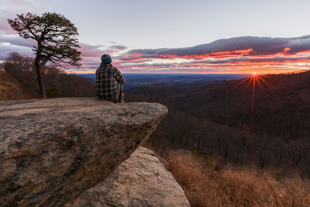 Man sitting on a cliff, watching sunset. Free public domain CC0 photo.