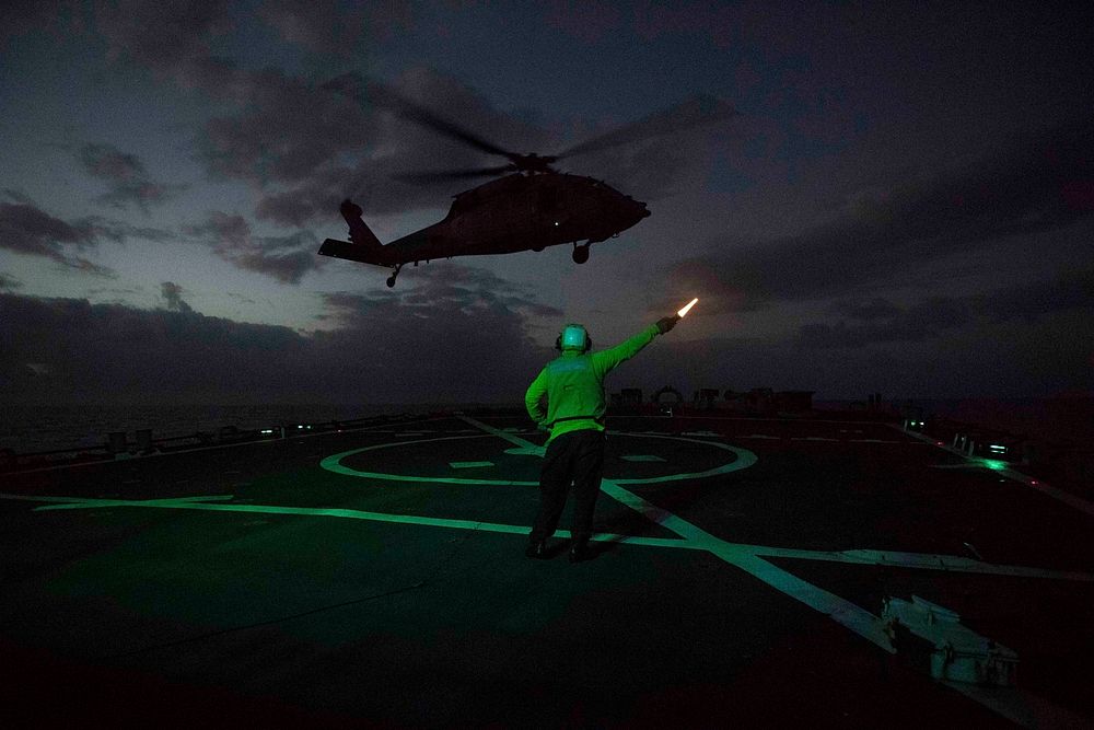 U.S. Navy Boatswain's Mate 1st Class Theodore Faison signals to an outgoing SH-60S Sea Hawk helicopter assigned to…