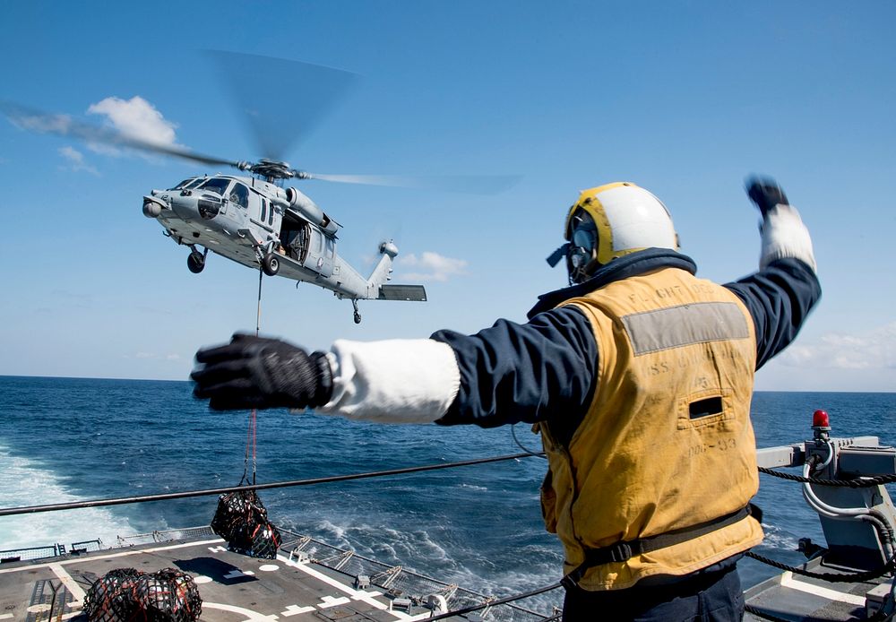 U.S. Naval landing signalman directs a helicopter during a vertical replenishment at sea in the sea of Japan aboard USS…