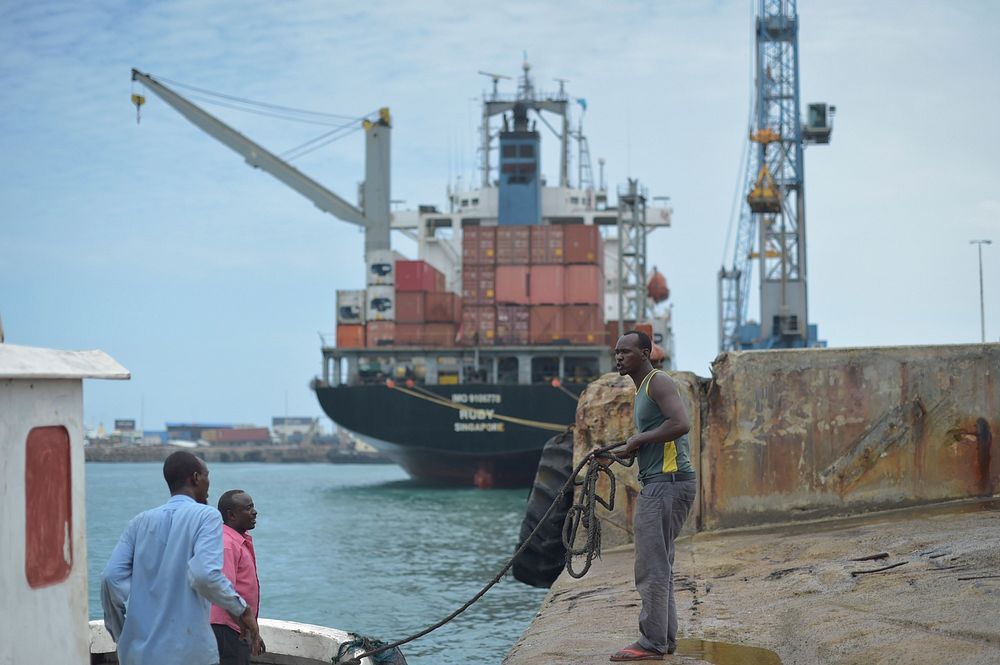 A Somali man helps dock a smaller boat in Mogadishu's port on September 17, 2005, while a much larger container ship gets…