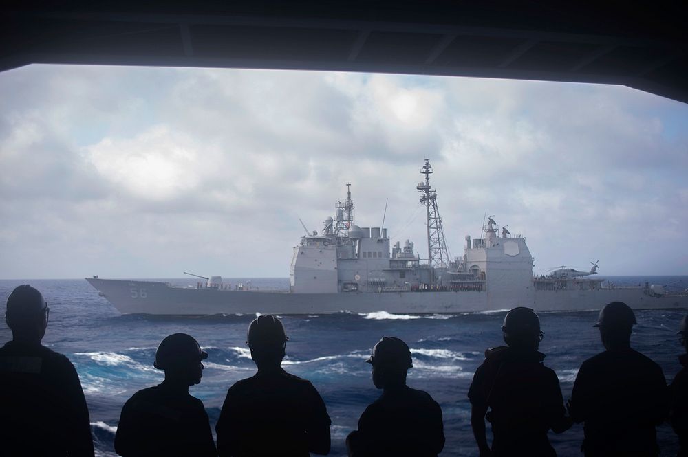 U.S. Sailors look out the hangar bay door of the aircraft carrier USS Dwight D. Eisenhower (CVN 69) as it pulls alongside…